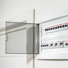 Otwarta biała skrzynka z bezpiecznikami elektrycznymi i przezroczystą klapką.