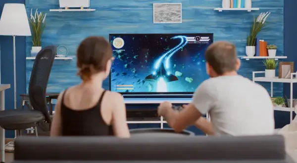 Para grająca w grę kosmiczną na dużym telewizorze.